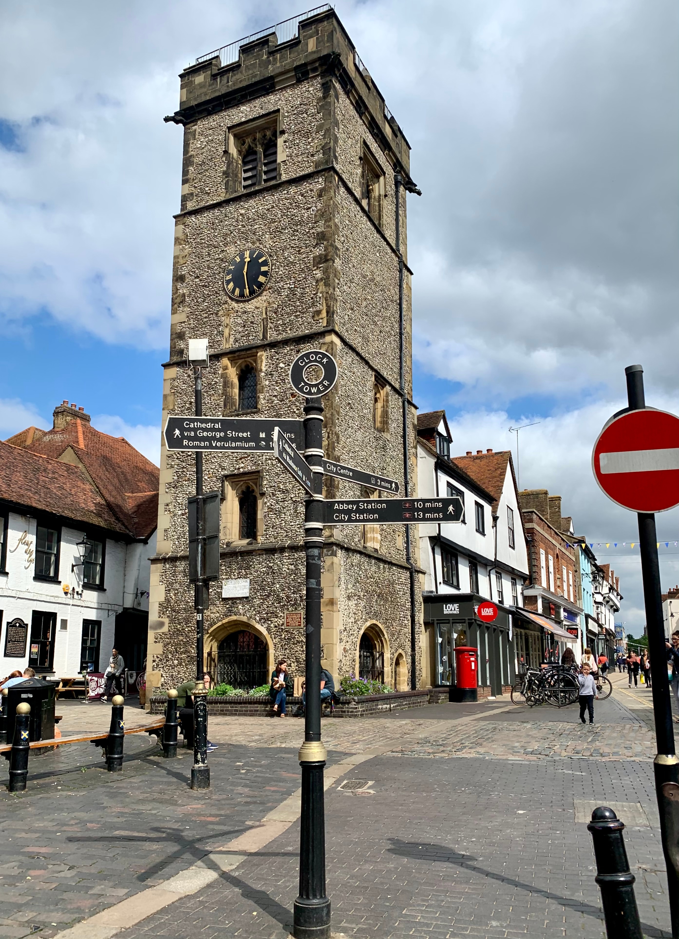 The medieval Clock Tower in St Albans city centre, standing above cobbled streets, historic buildings and signposts for the cathedral and Roman Verulamium.